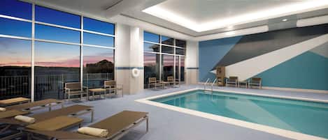 A pool area with lounge chairs, a pool, and large windows offering a view of the sunset.