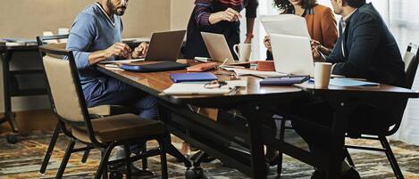 A conference room with a long table, laptops, and people engaged in discussion.