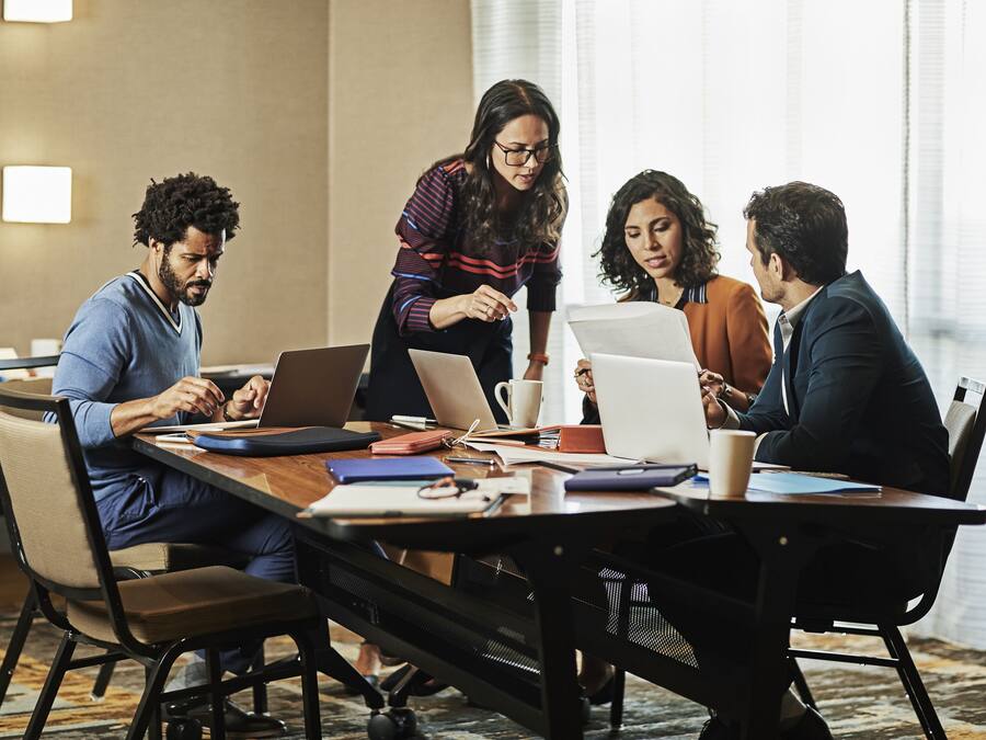 A conference room with a long table, laptops, and people engaged in discussion.