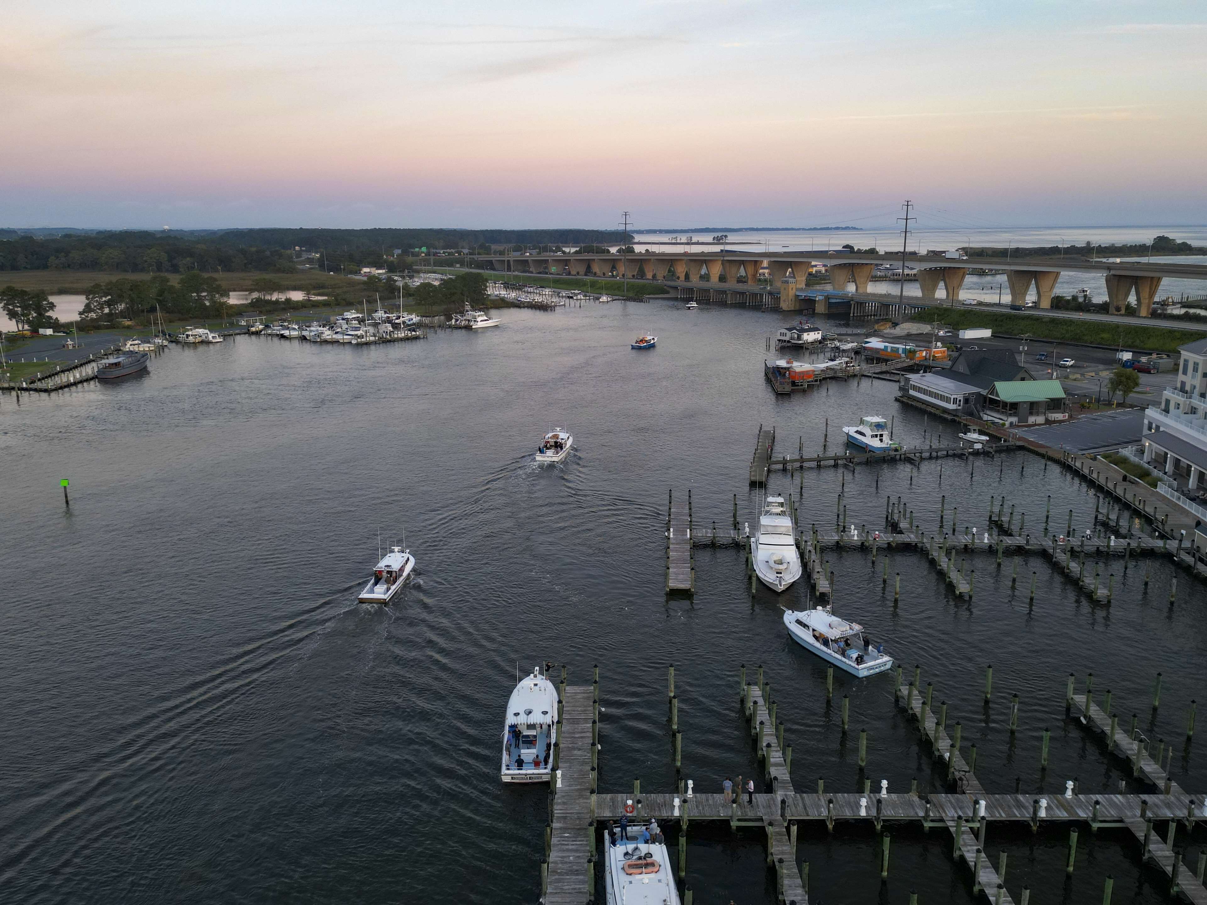 A marina with boats docked, a bridge in the background, and a waterfront view.