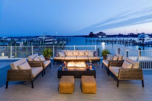 Une terrasse sur le toit, aménagée avec des meubles en osier, un foyer et offrant une vue sur un port de plaisance.