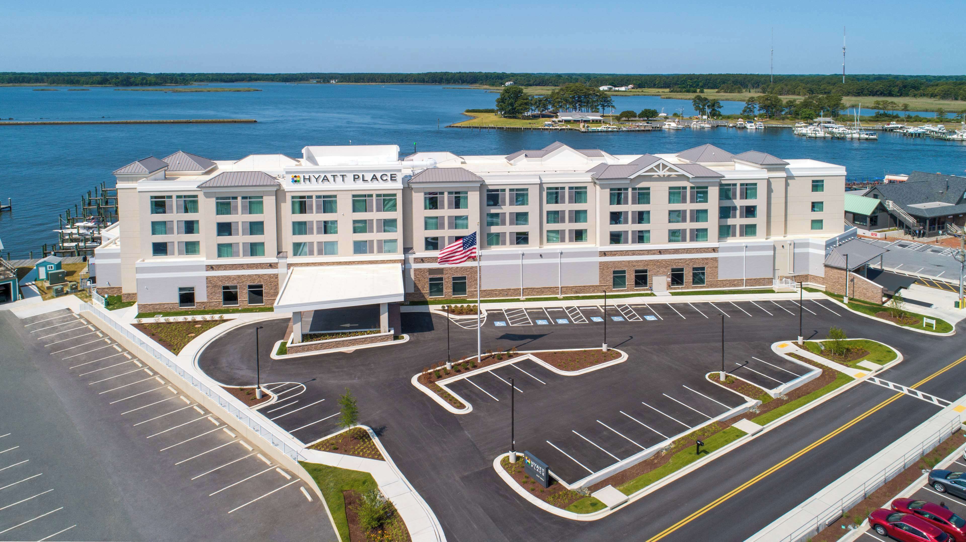 A Hyatt Place hotel with a parking lot, a flag, and a marina in the background.