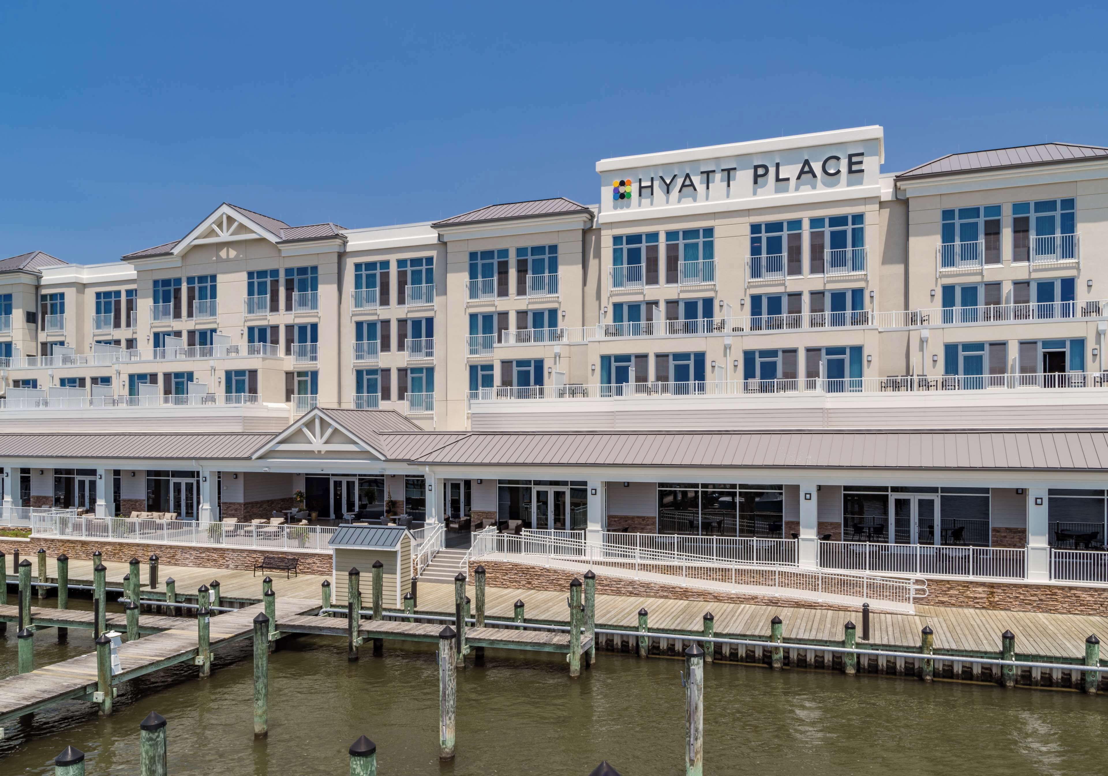 Un hotel de varios pisos con un llamativo letrero de "HYATT PLACE", ubicación frente al agua y un pasillo cubierto que conecta con el muelle.