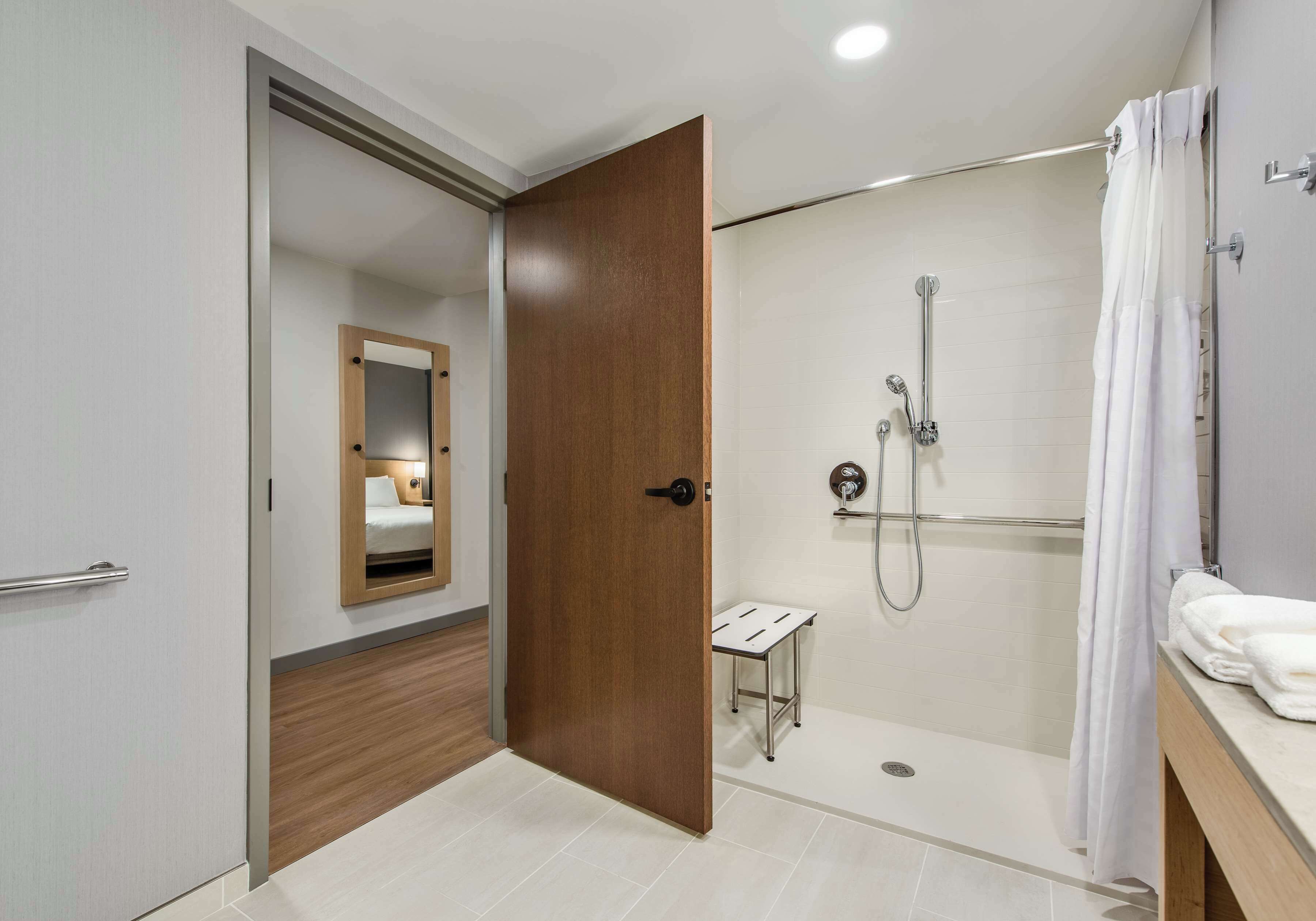 A modern bathroom with a walk-in shower, a wooden door, and a small vanity table.