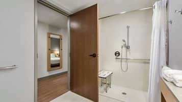 A modern bathroom with a walk-in shower, a wooden door, and a small vanity table.