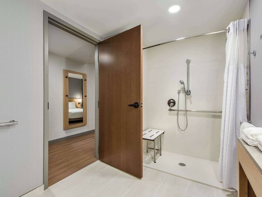 A modern bathroom with a walk-in shower, a wooden door, and a small vanity table.