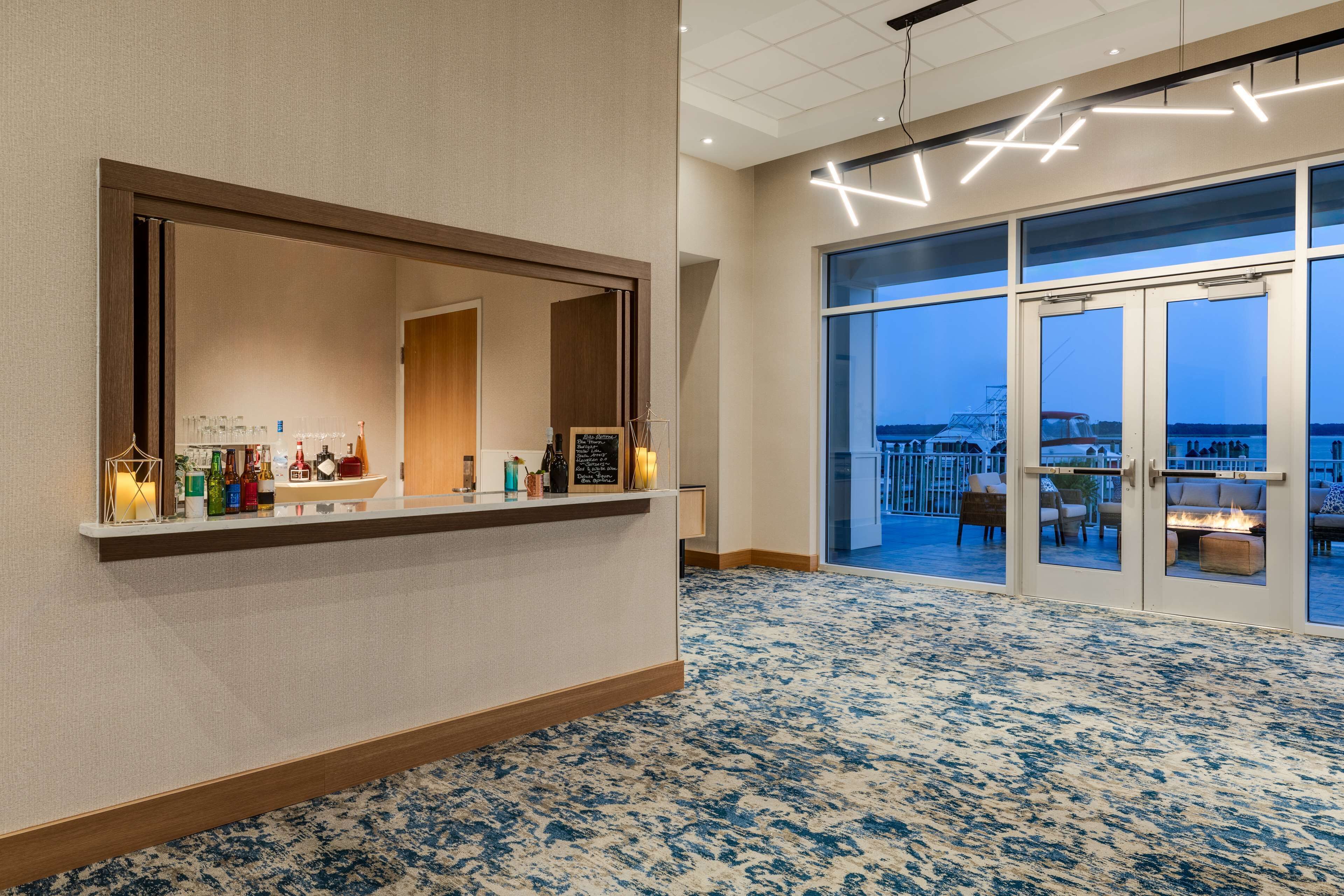 A hotel lobby with a reception desk, a large mirror, and a view of the sea through large glass doors.