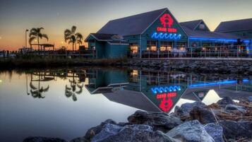 Un edificio frente al agua con un letrero de neón que dice "CRAB DECK" y un reflejo en el agua.