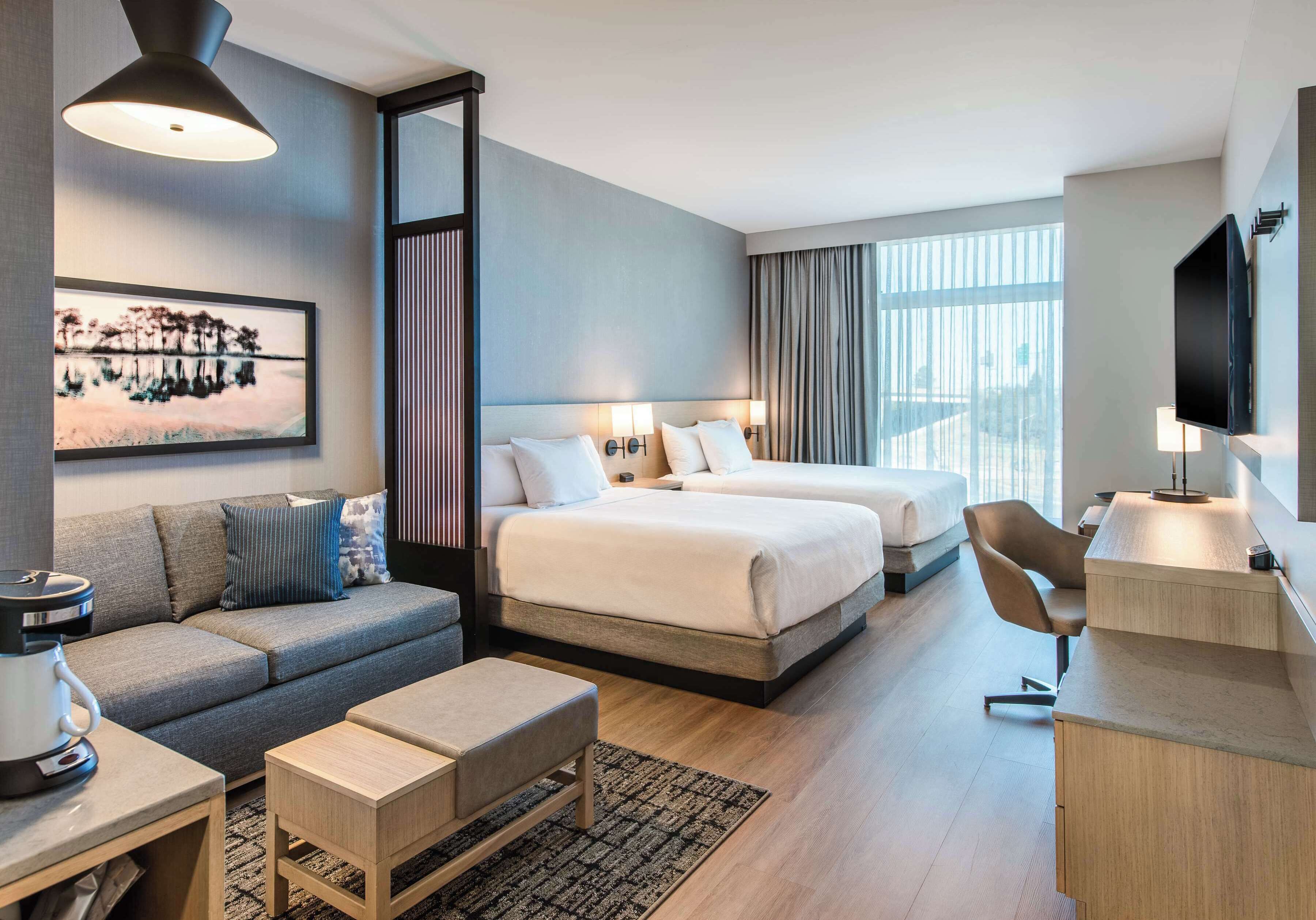Een moderne hotelkamer met twee bedden, een sofa, een bureau en een televisie.