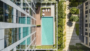 Ein Pool auf dem Dach mit Glasbarriere, umgeben von Grünpflanzen und neben einem modernen Gebäude.