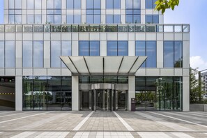 Un edificio moderno con fachada de vidrio, entrada cubierta y suelo de baldosas.
