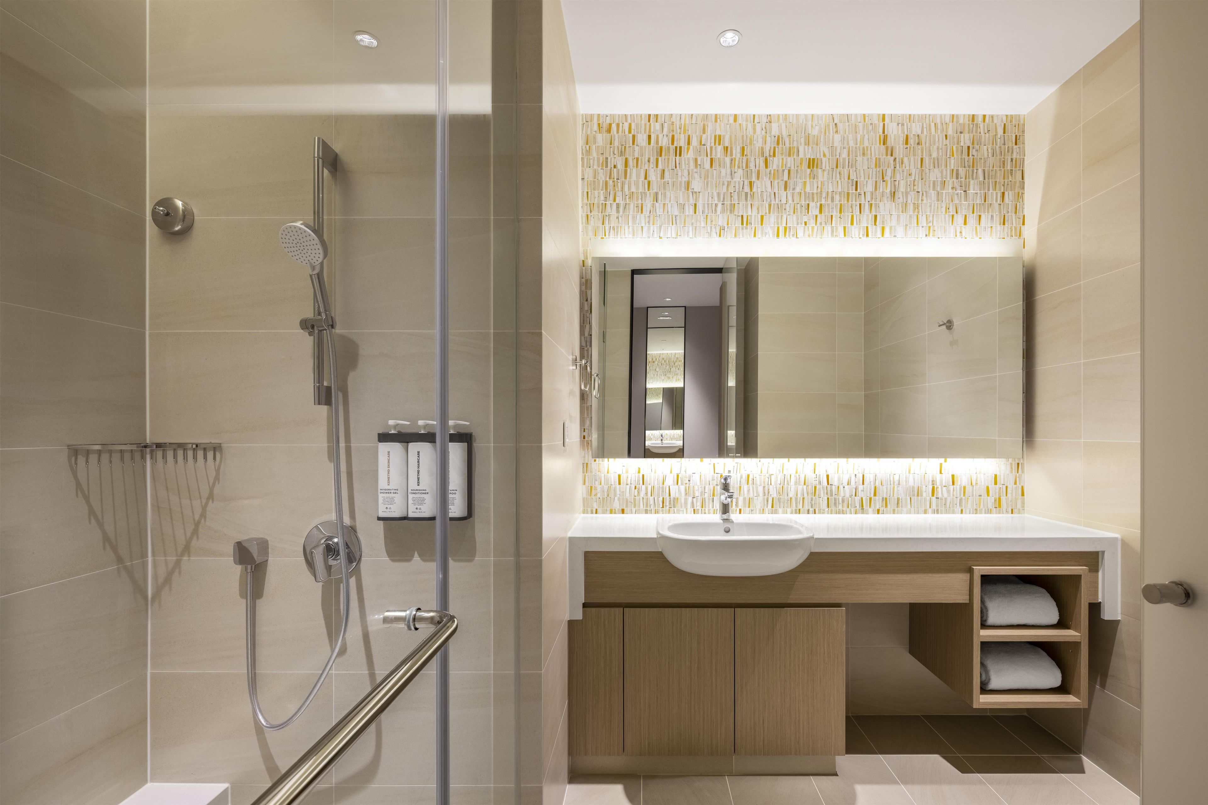 A modern bathroom with a glass shower enclosure, a sink with a mirror above, and a towel shelf.