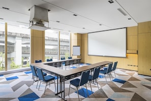A conference room with a large table, chairs, a projector screen, and a view of an outdoor area.