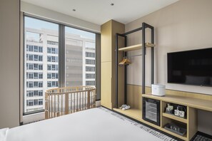 Ein modernes Hotelzimmer mit großem Fenster, einem Kinderbett, einem Fernseher und einer Holzkonsole mit Regalen.