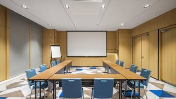 A conference room with a long table, blue chairs, a projector screen, and a whiteboard.