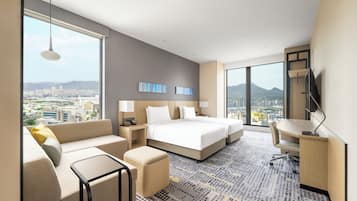 A hotel room with a large bed, a sofa, a desk, and a view of the city.