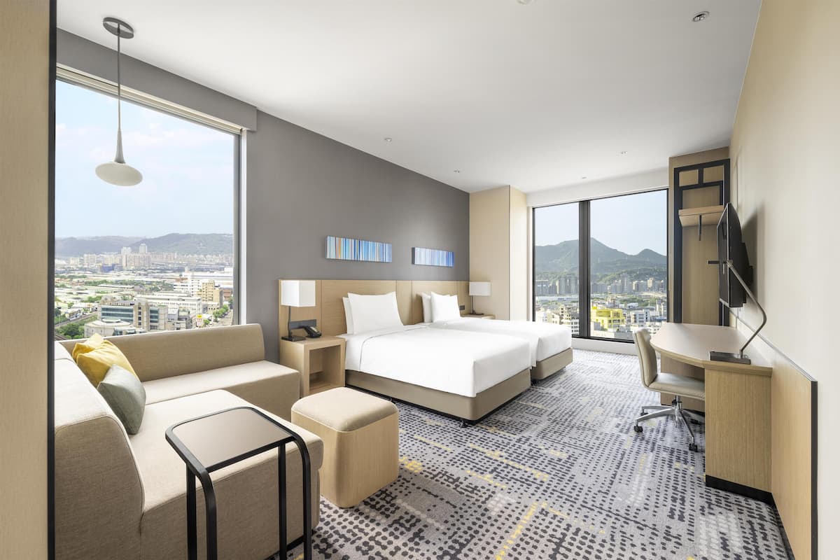 A modern hotel room with a large bed, a sofa, a desk, and a view of the city.