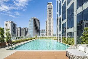 Una piscina en la azotea con cubierta de madera, rodeada de edificios modernos y vegetación.