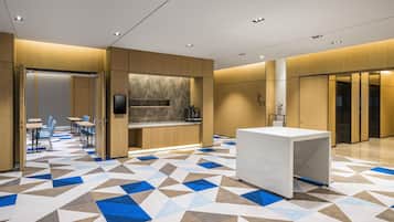 A modern hotel lobby with a geometric patterned floor, a reception desk, and a seating area with tables and chairs.