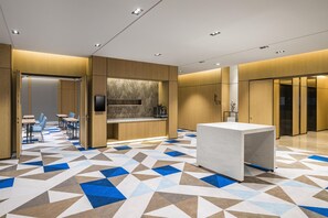 Un vestíbulo moderno de hotel con piso de diseño geométrico, un mostrador de recepción y una zona de estar con mesas y sillas.