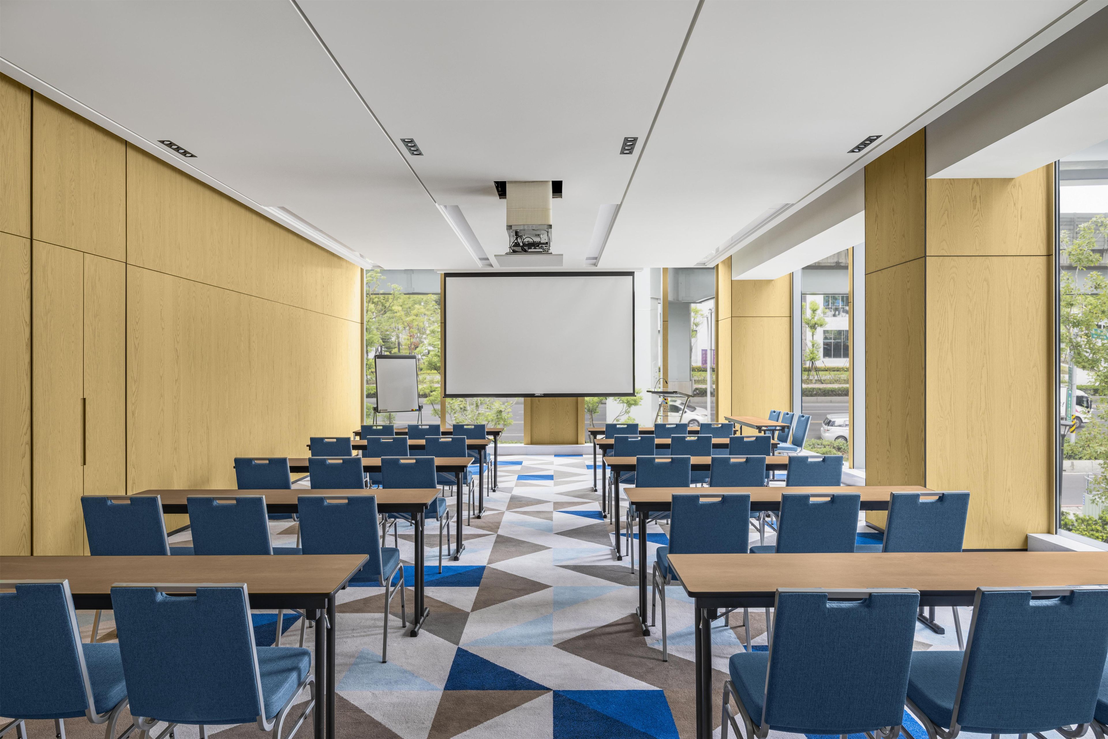 A conference room with a large screen, blue chairs, and a geometric patterned carpet.