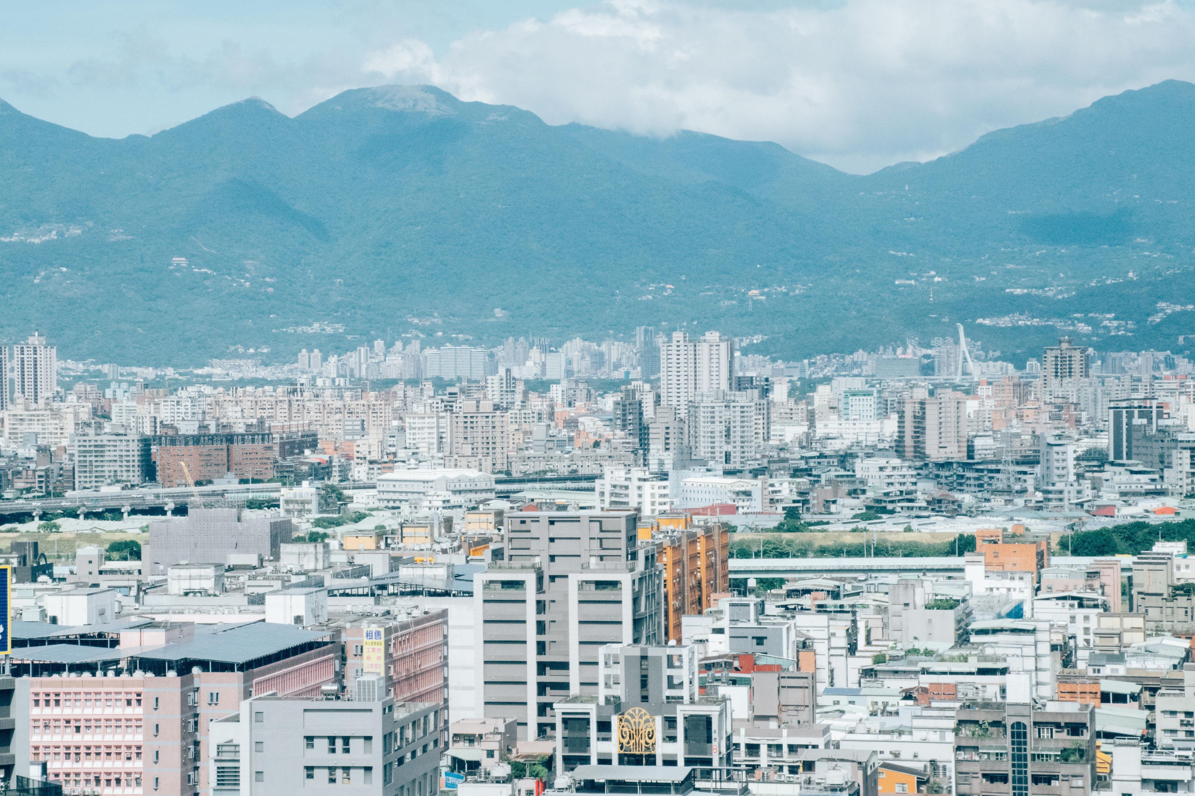 Un paisaje urbano con un denso conjunto de edificios, un puente y montañas al fondo.