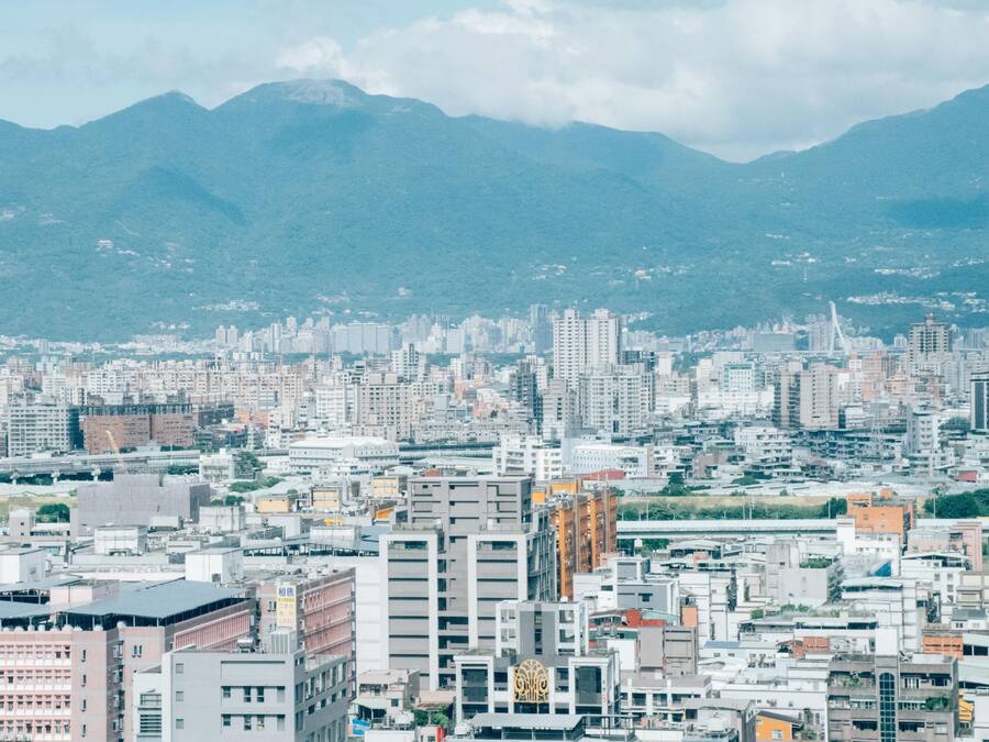 A cityscape with a dense cluster of buildings, a bridge, and mountains in the background.