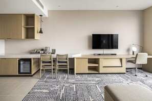 Eine moderne Küche mit Backofen, ein Essbereich mit zwei Stühlen, ein an der Wand befestigter Flachbildfernseher und ein kleiner Schreibtisch mit Stuhl.