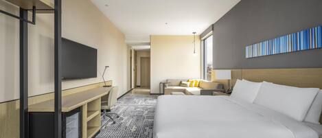 Quarto de hotel com uma cama grande, uma escrivaninha, televisão e vista para a cidade.