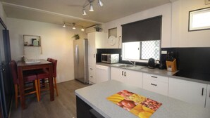 Cozinha compacta com geladeira, micro-ondas e cafeteira. Há uma mesa de jantar com cadeiras e um relógio na parede.