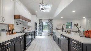 Une cuisine moderne avec des meubles blancs, un îlot central et une vue sur l’extérieur.
