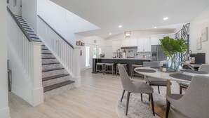 Une cuisine spacieuse dotée d’un îlot central, un coin repas avec une table ronde et des chaises, et un escalier menant à un autre niveau.