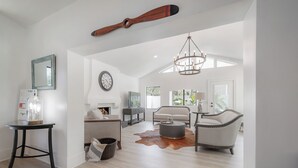 Un vaste espace de vie au design moderne, agrémenté d’une poutre en bois au plafond, d’un lustre et d’un grand tapis en peau de vache.