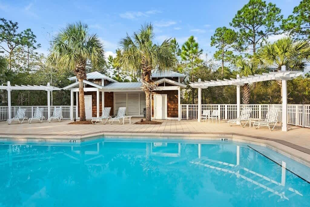 Una piscina con sillones de descanso y una zona cubierta con pérgola.