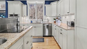 Una cocina moderna con armarios blancos, electrodomésticos de acero inoxidable y una ventana con vistas a árboles.