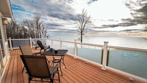 Una terraza de madera con mobiliario exterior, barandilla y vista a un cuerpo de agua.