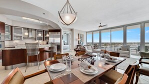 A modern kitchen with a dining area, large windows, and a view of the city. - Bella Luna 1009-Luxury Condo-Great Views-Walk to Flora-Bama-Boaters Heaven! (Orange Beach)