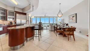 A modern kitchen with a central island, stainless steel appliances, and a dining area with a view. - Bella Luna 1009-Luxury Condo-Great Views-Walk to Flora-Bama-Boaters Heaven! (Orange Beach)