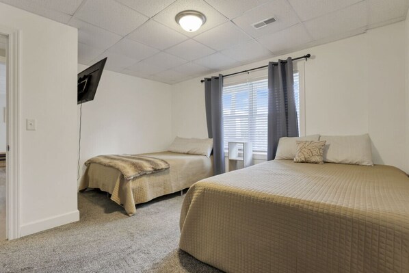 Un dormitorio con dos camas, un televisor de pantalla plana en la pared y una ventana con cortinas.