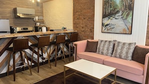 Un espace de vie moderne comprenant un coin cuisine, un bar avec des tabourets, un canapé rose et un tableau accroché au mur.