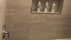 Une salle de bain avec un mur carrelé et une étagère sur laquelle sont posées trois bouteilles.