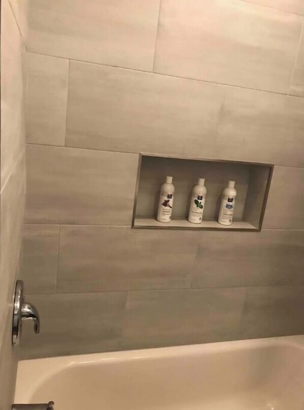 A bathroom with a tiled wall and a shelf holding three bottles.