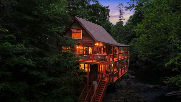 A wooden cabin with a balcony, surrounded by dense forest.