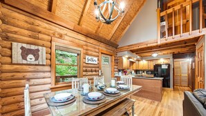 A wooden cabin interior with a dining area, kitchen, and a loft bedroom.