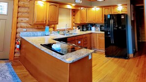 A log cabin-style kitchen with wooden cabinets, granite countertops, a built-in stove, and a black refrigerator.
