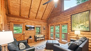 A log cabin interior with a sofa, a table, and a painting of a forest.