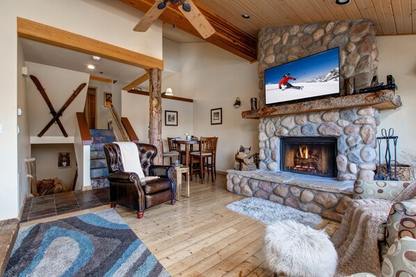 A cozy living room with a stone fireplace, a television mounted above it, and a ski-themed decor including skis and a ski helmet.