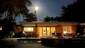 Un bâtiment doté d’une piscine, de palmiers et où l’on peut admirer la lune dans le ciel.