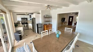 Une cuisine spacieuse avec des meubles blancs, une table à manger en bois et un ventilateur de plafond.