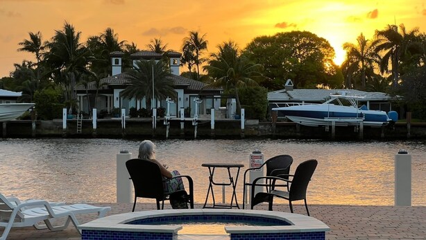 Un espace piscine comprenant un jacuzzi, des chaises longues et une vue sur une marina avec des bateaux et une maison en arrière-plan.
